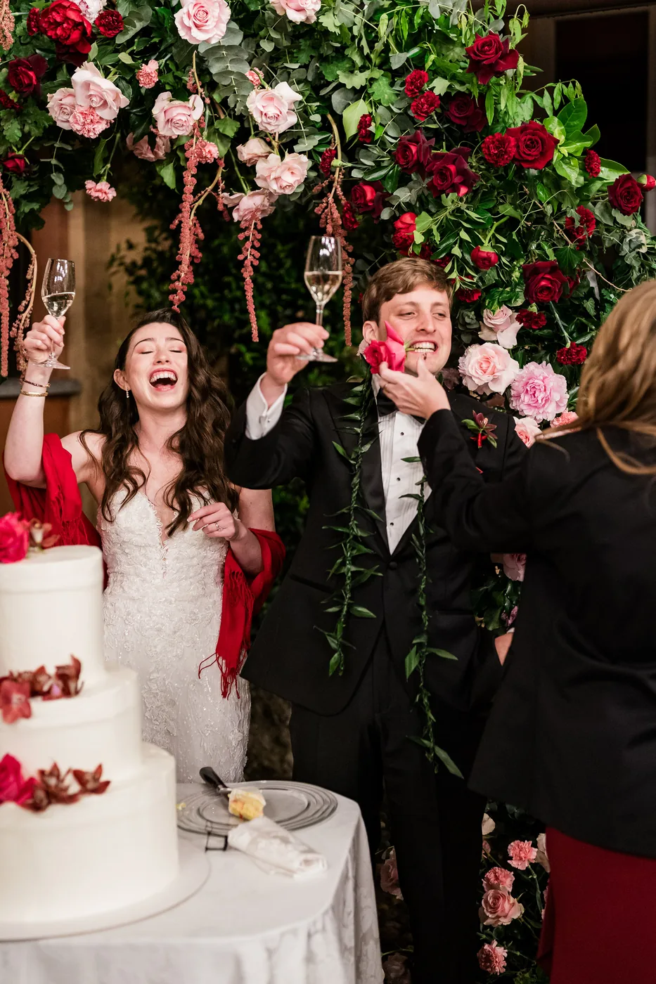 Reviews 2 The couple laugh and toast in front of a rose arch at the cake cutting